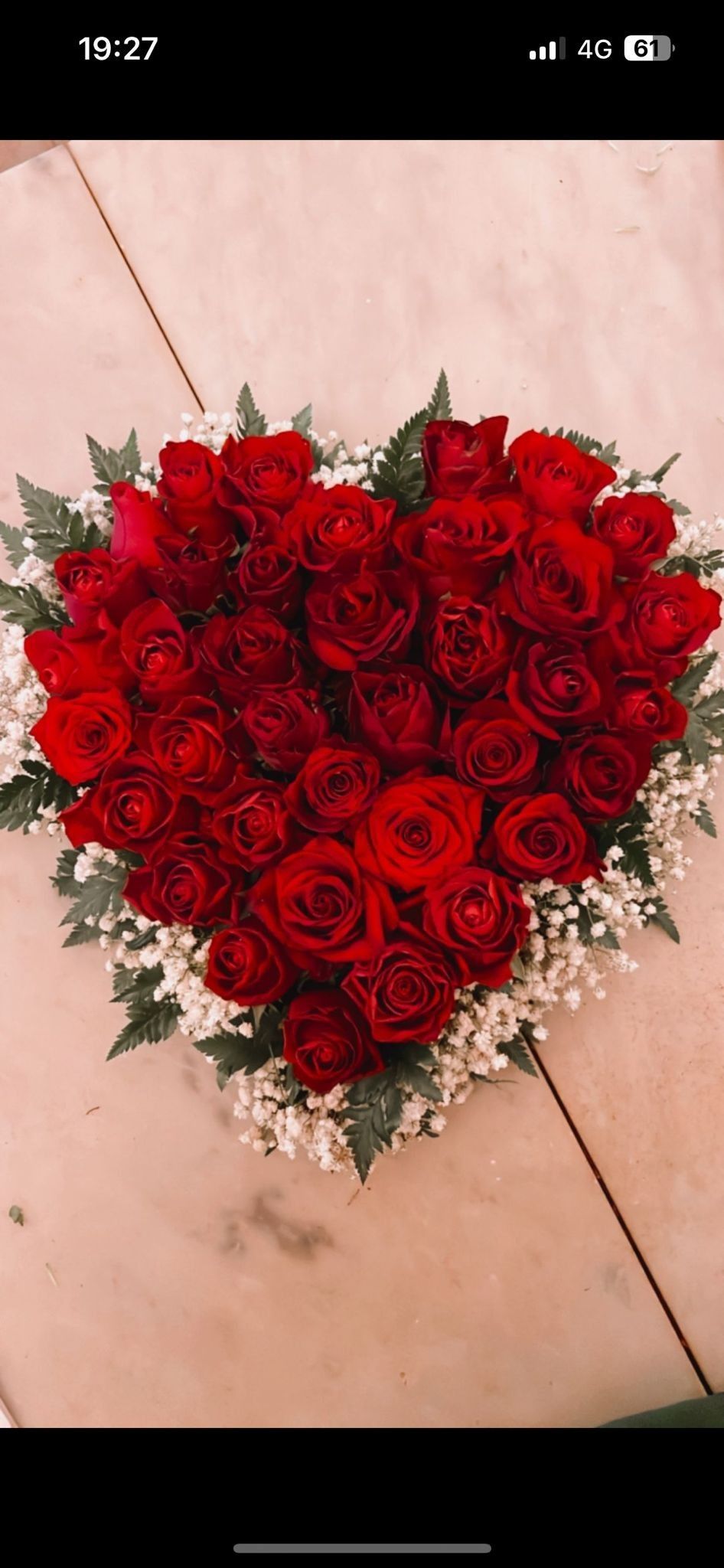 Una composizione a forma di cuore di rose rosse circondate da verde e piccoli fiori bianchi.