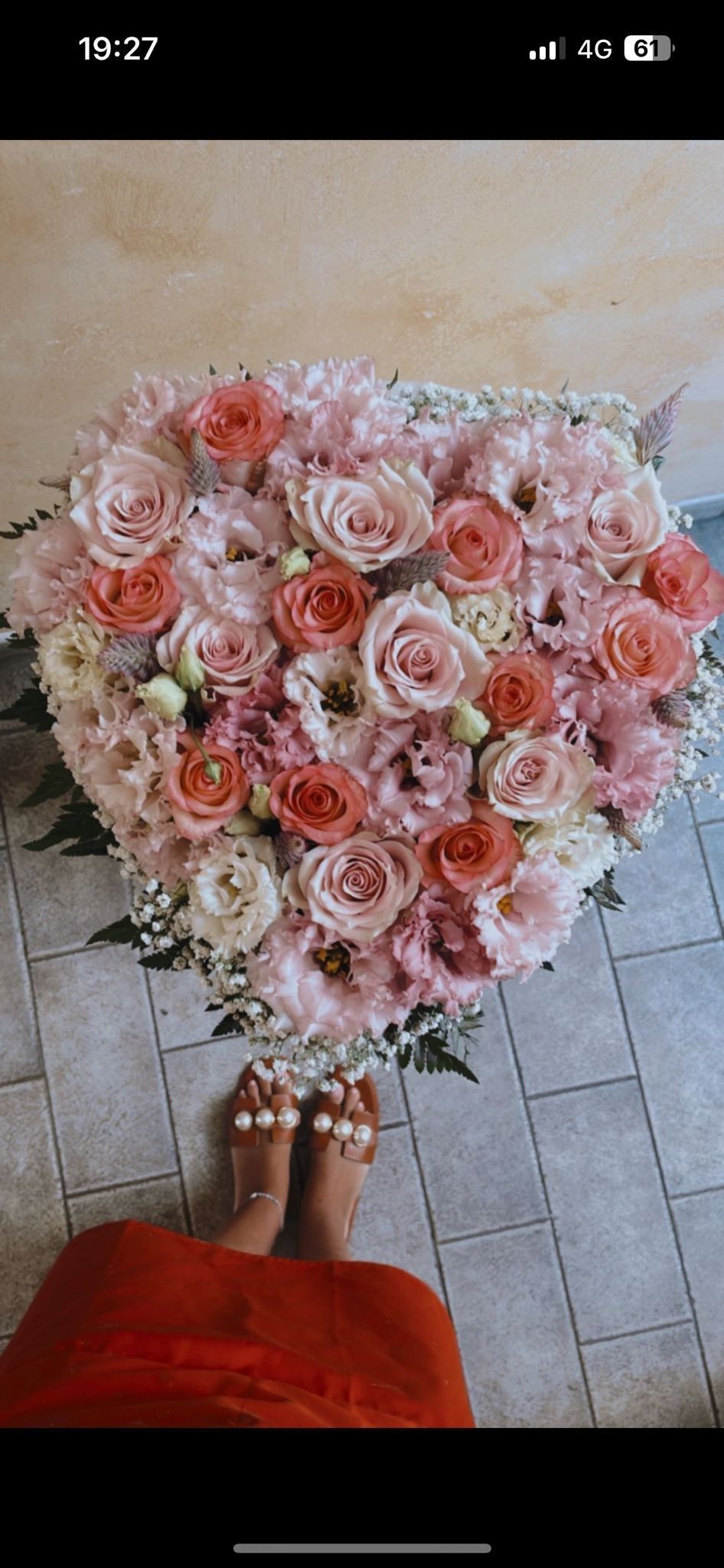 Grande mazzo di fiori rosa e pesca con i piedi nei sandali sotto.