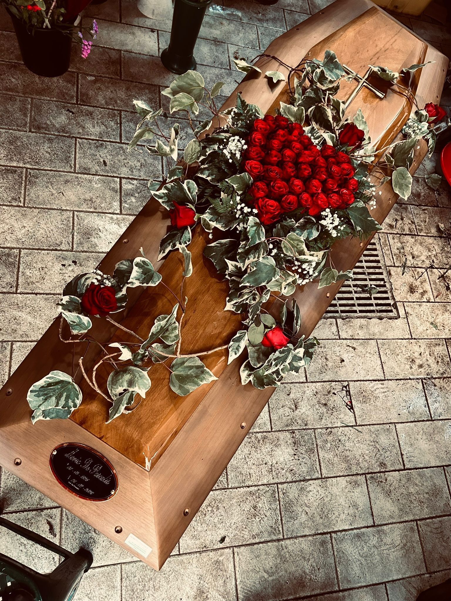Una bara di legno con una composizione floreale: cuore rosso, rose rosse, edera su un pavimento di mattoni.