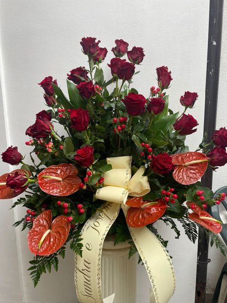 Composizione floreale con rose rosse e anthurium, nastro color crema, in un vaso.