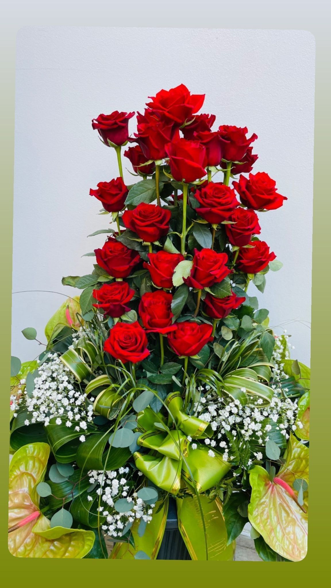 Bouquet di rose rosse con verde e un grande nastro verde.