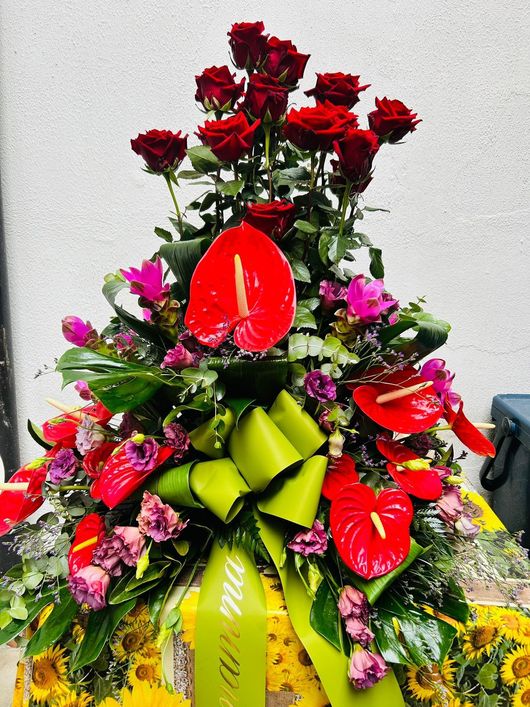 Composizione floreale di rose rosse e anthurium con nastro verde.
