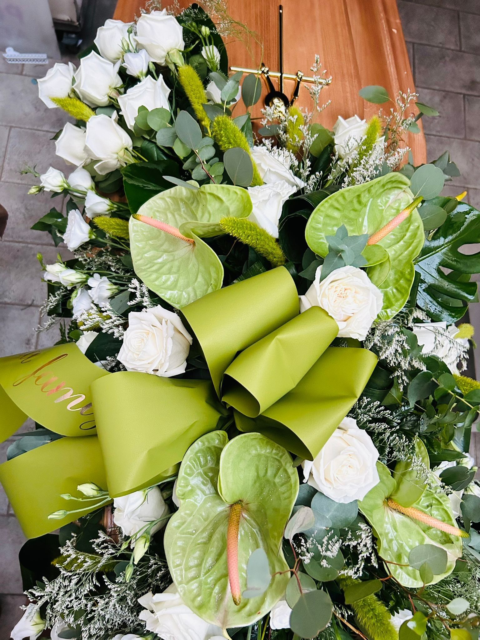 Composizione floreale verde e bianca sopra una bara di legno, con rose e anthurium.