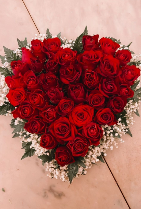 Composizione floreale con fiori rosa e verdi, impreziosita da un nastro verde e steli alti, contro una parete bianca.