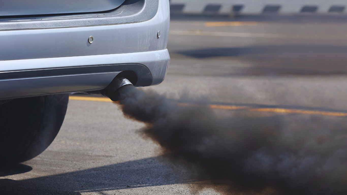 A vehicle exhaust pipe emitting a thick cloud of black smoke on an asphalt road.