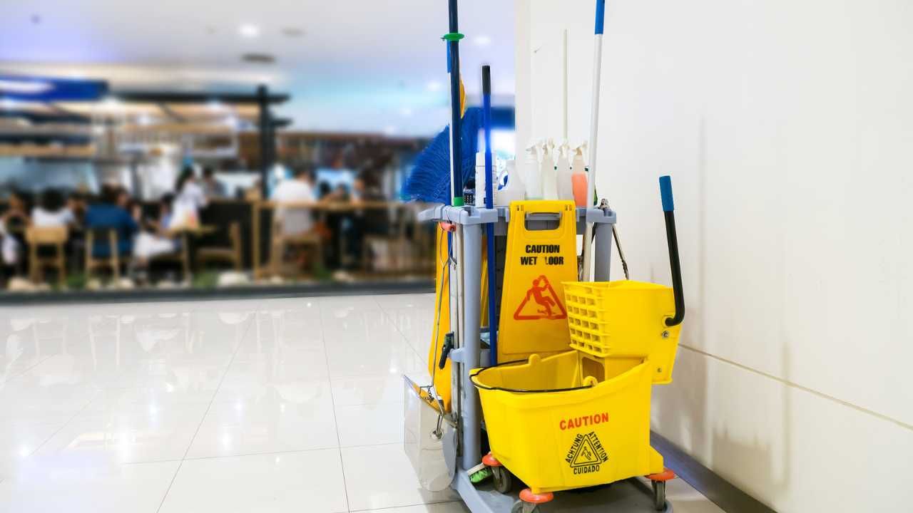 A yellow cleaning cart equipped with mops and buckets.