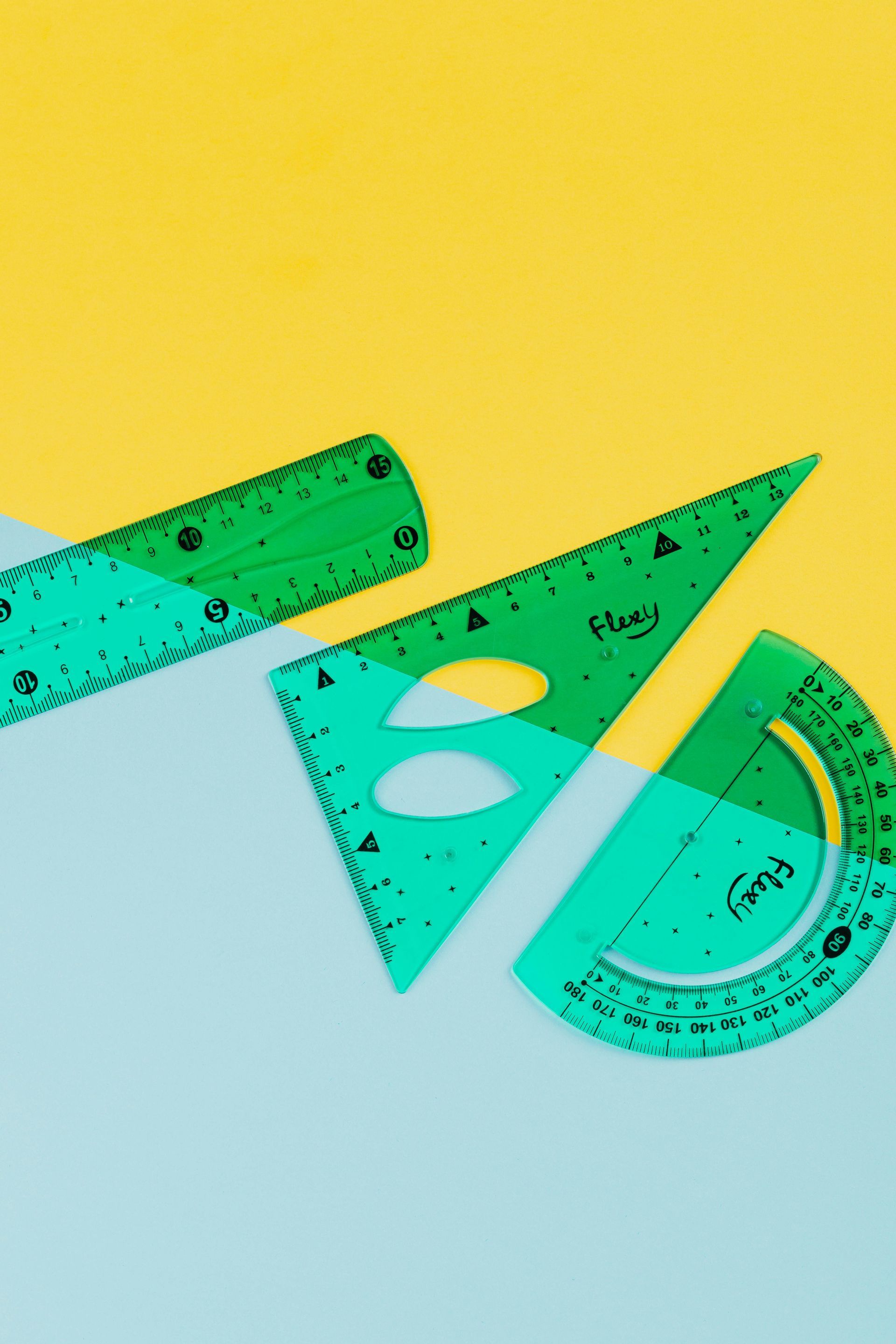 Reglas verdes, triángulo y transportador sobre fondo amarillo y azul.