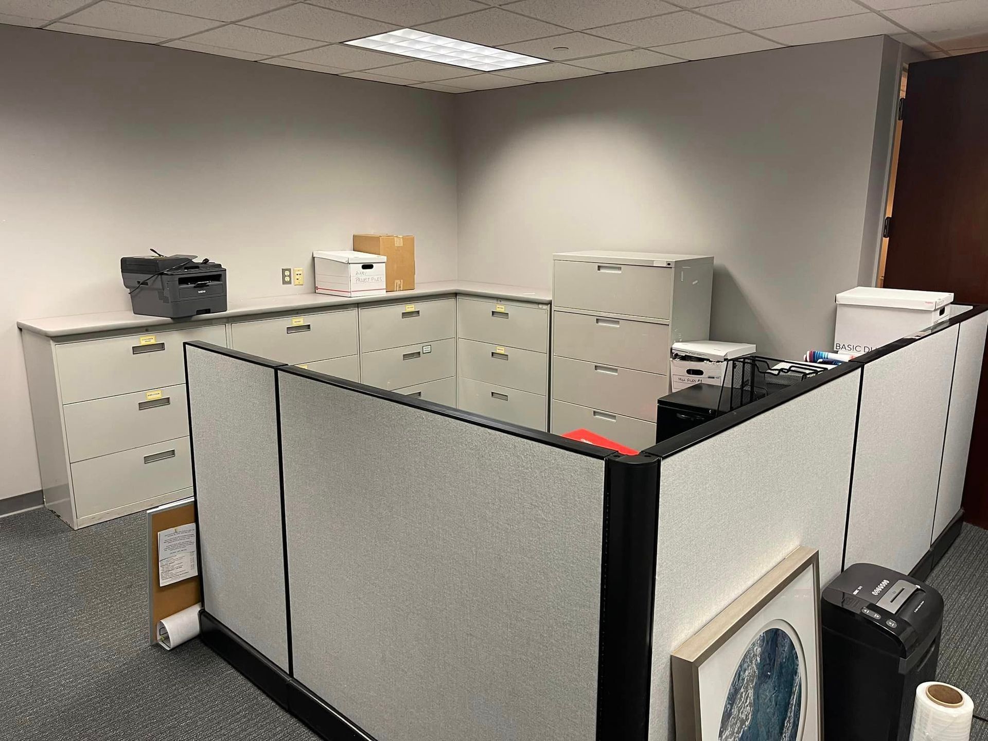 A cubicle in an office with a printer and filing cabinets.