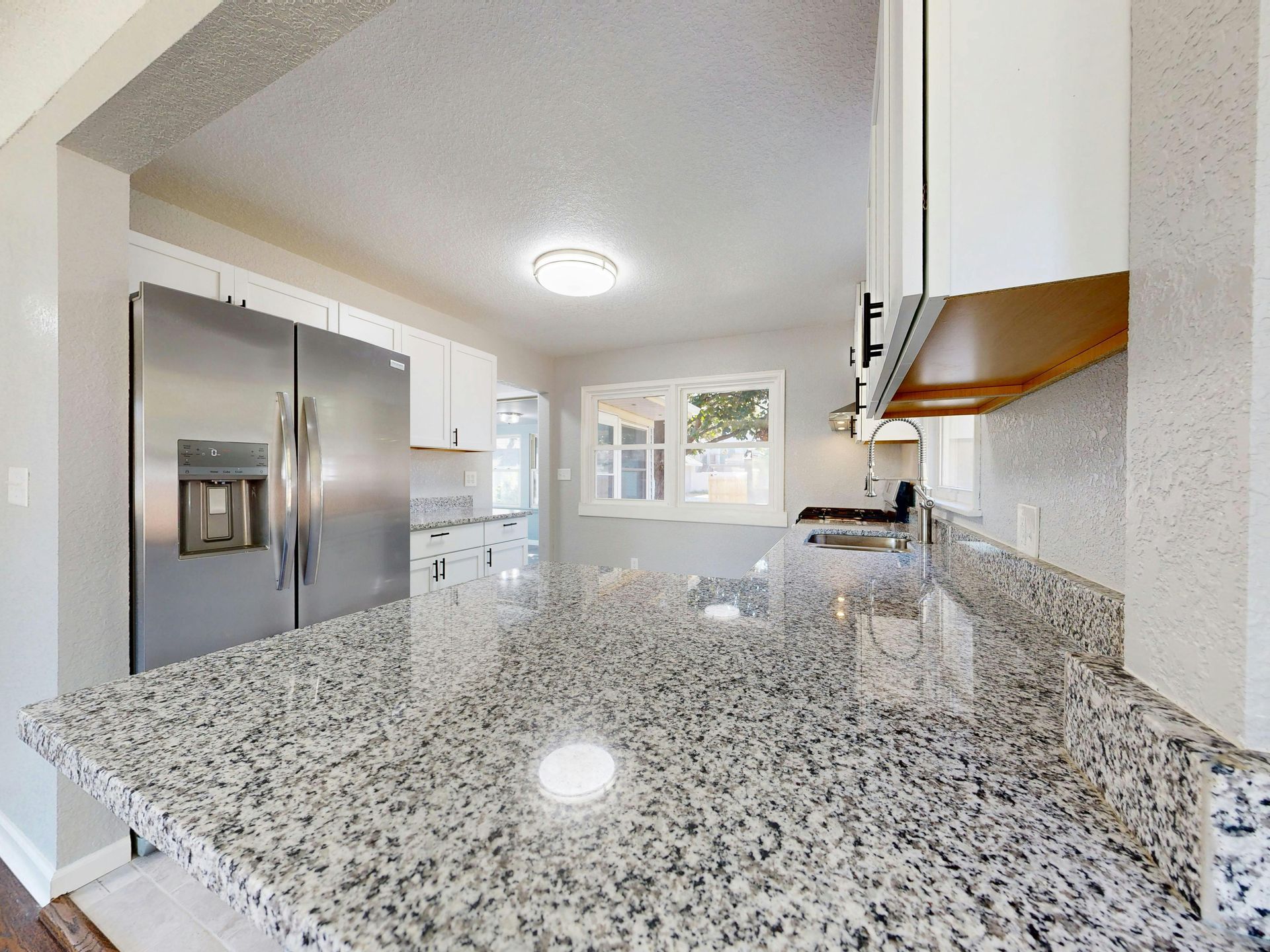 A modern kitchen features granite countertops, stainless steel appliances, and white cabinets under bright lighting.