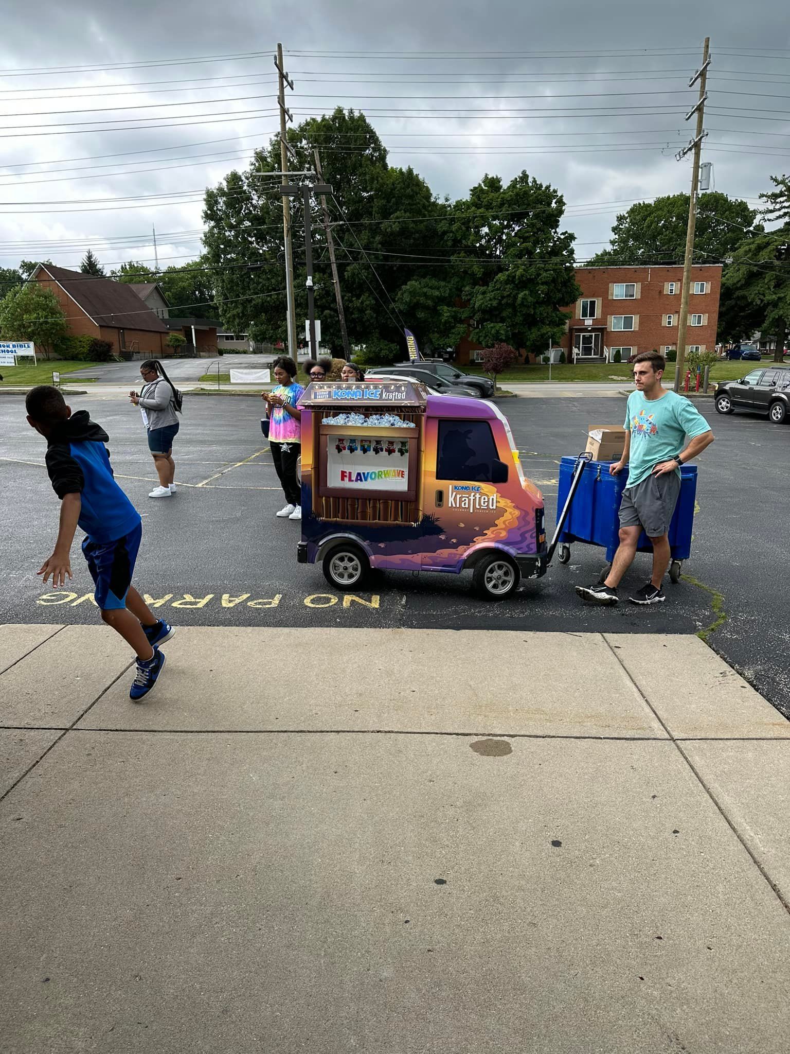 A group of people are standing around a toy car in a parking lot.