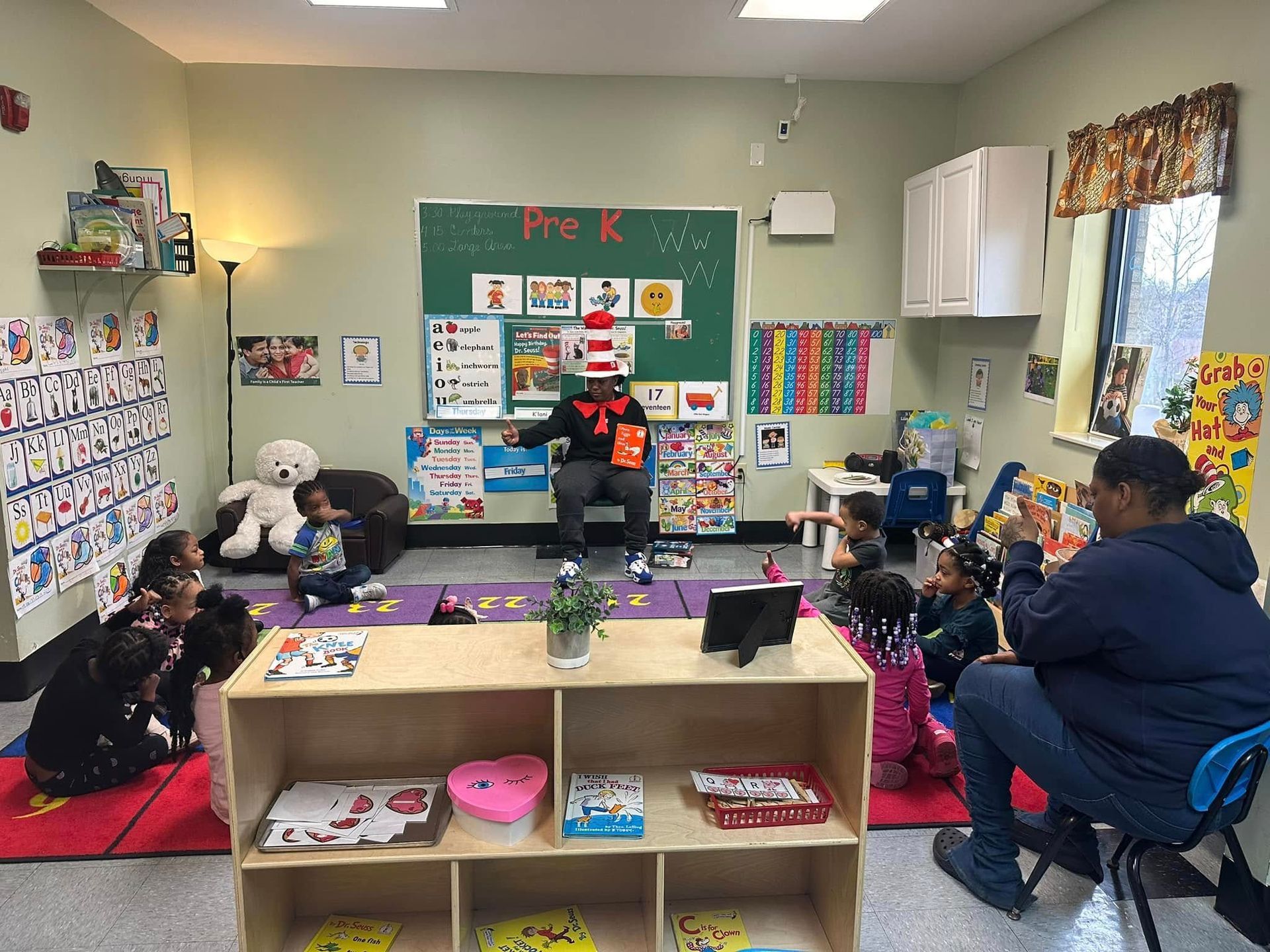 A man in a cat in the hat outfit is reading a book to a group of children in a classroom.