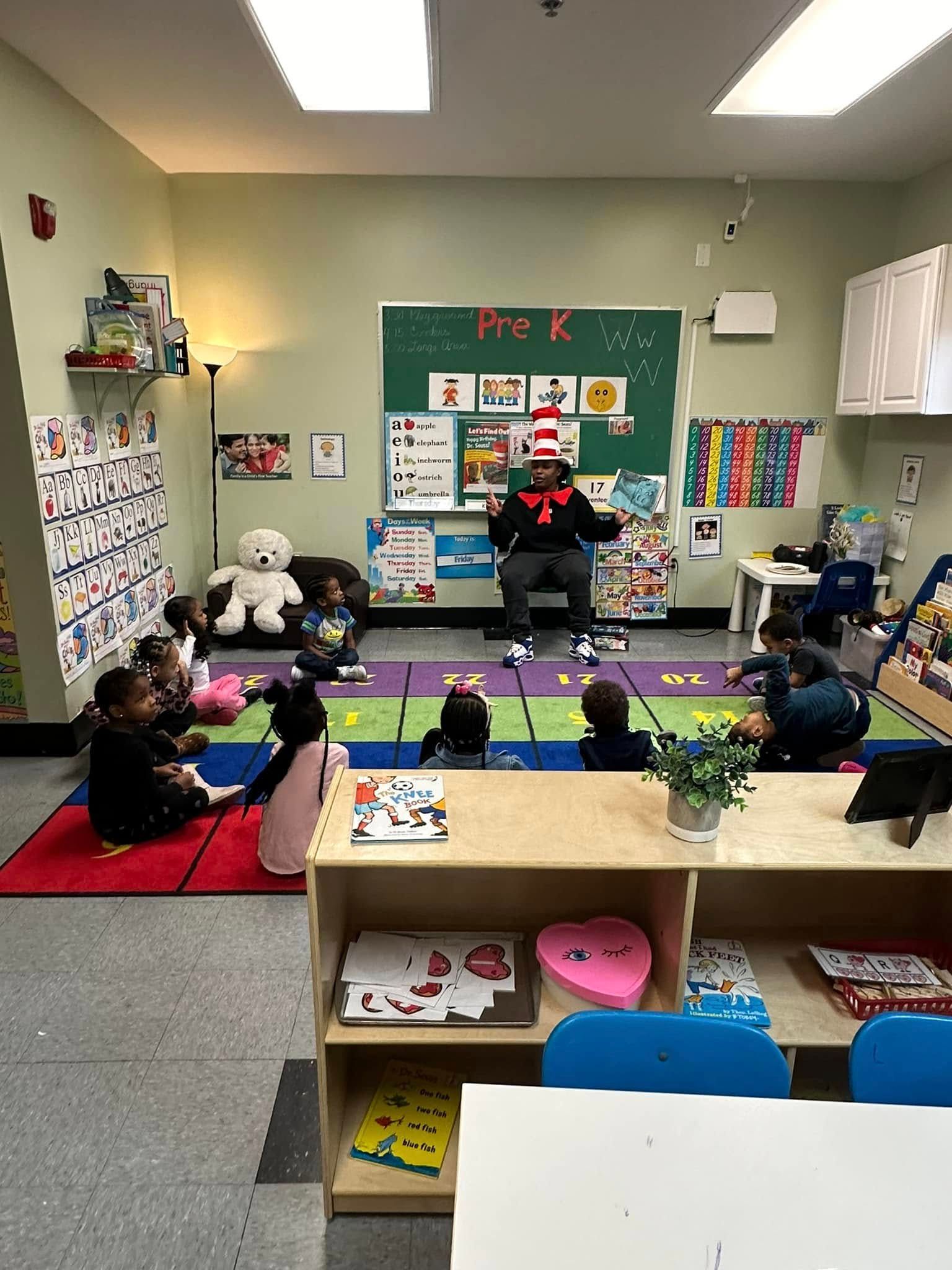 A man in a cat in the hat outfit is reading a book to a group of children in a classroom.