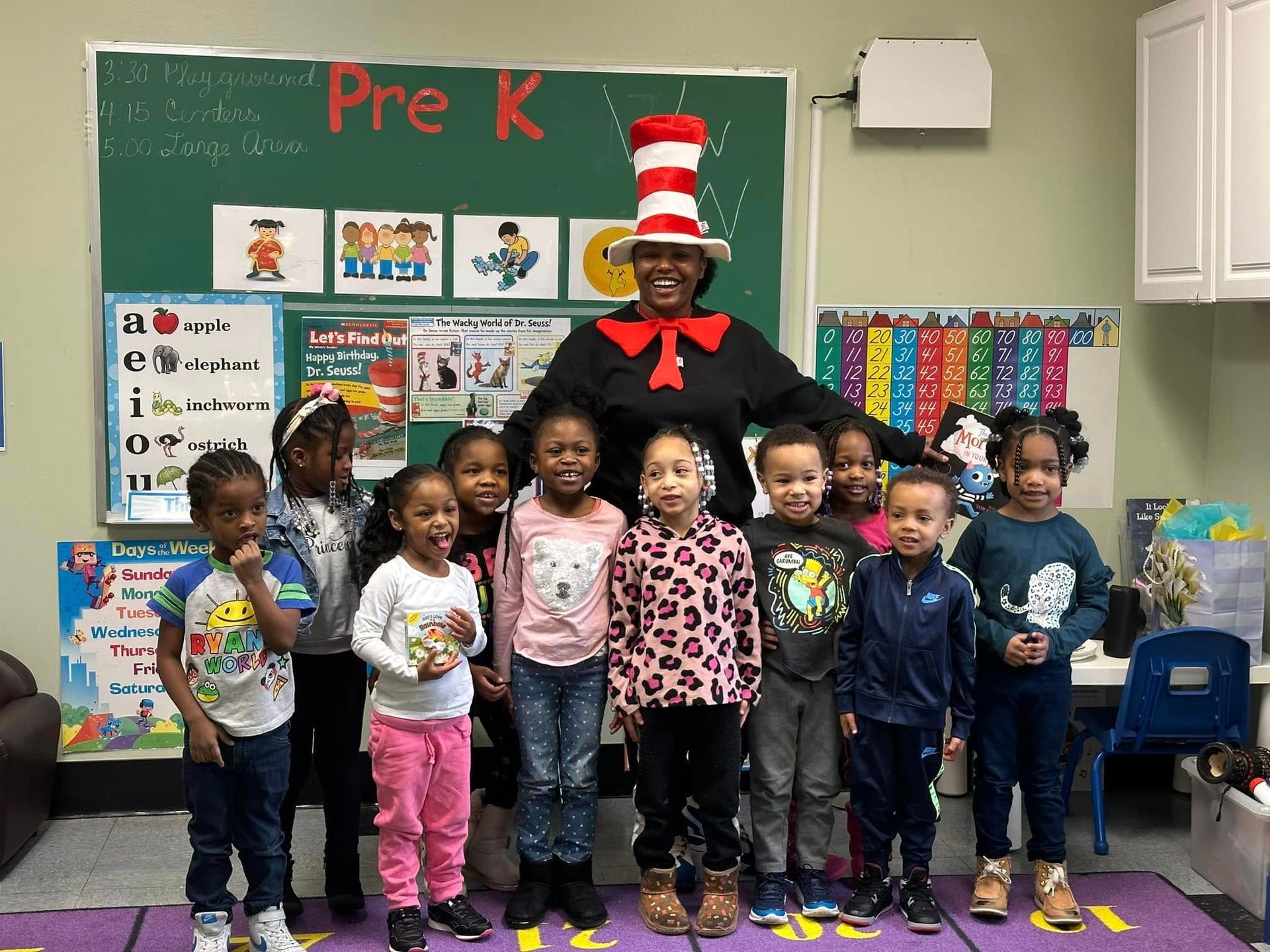 A group of children are posing for a picture with a man in a cat in the hat outfit.
