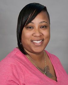 A woman wearing a pink shirt and a gold necklace is smiling for the camera.