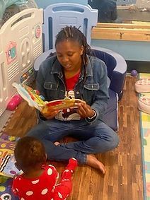 A woman is sitting on the floor reading a book to a baby.
