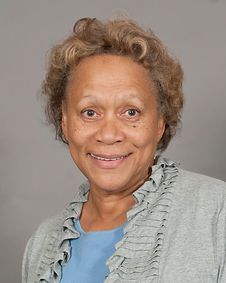 A woman in a blue shirt and gray sweater is smiling for the camera.