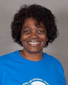 A woman with curly hair is wearing a blue shirt and smiling.