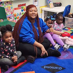 A woman is sitting on the floor with two little girls.