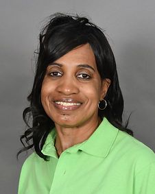 A woman wearing a green polo shirt and earrings is smiling for the camera.