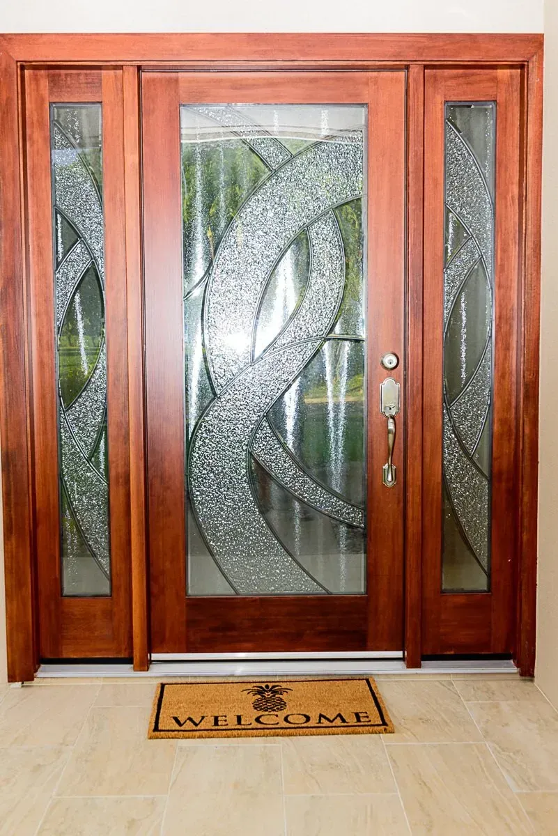 A wooden door with stained glass and a welcome mat in front of it.