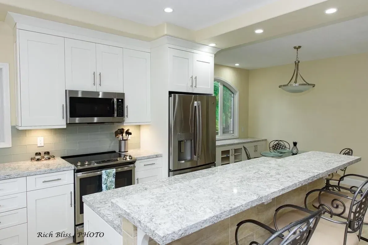 A kitchen with white cabinets , granite counter tops , stainless steel appliances and a large island.