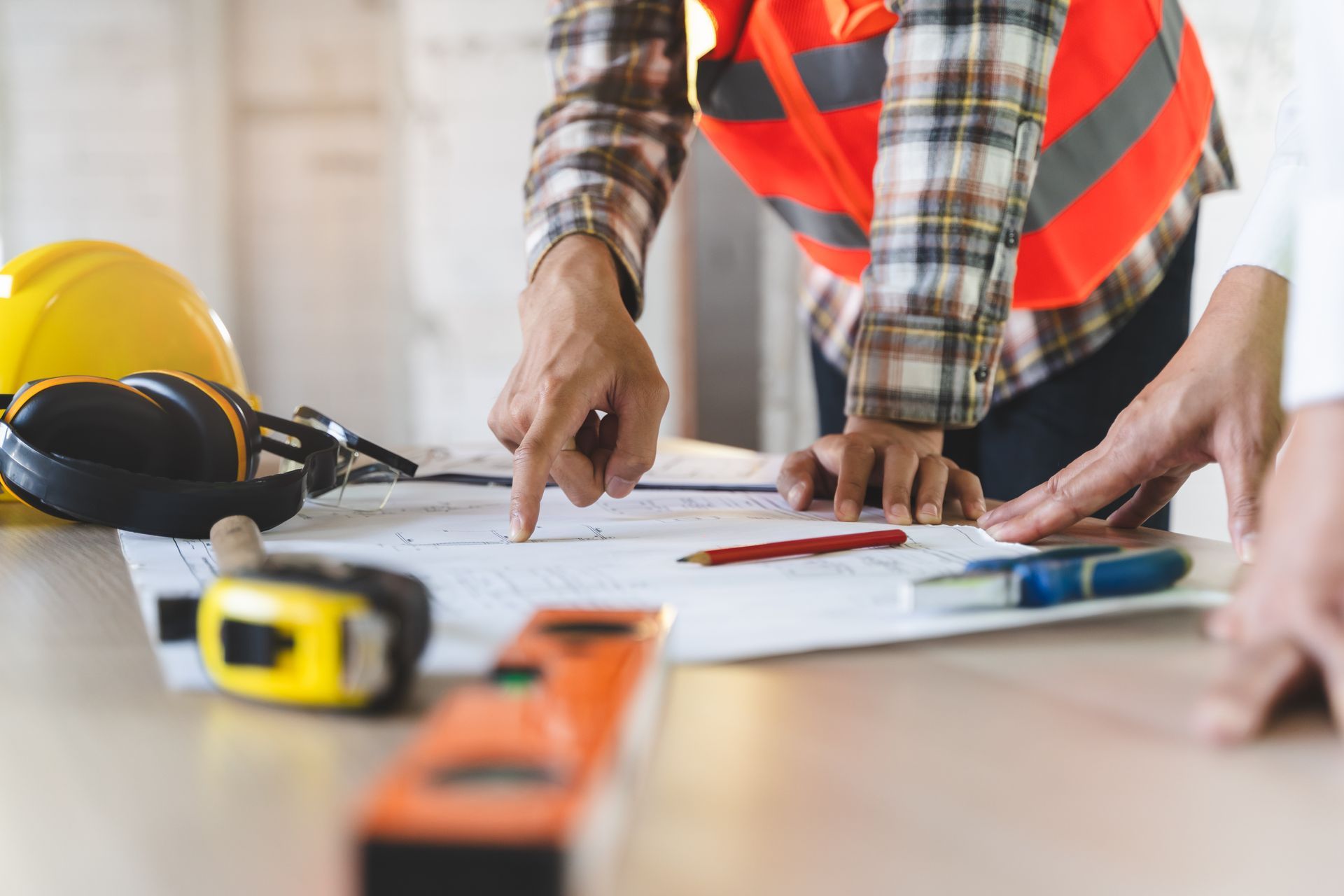 Construction professionals reviewing building plans on a table with safety gear and measuring tools.