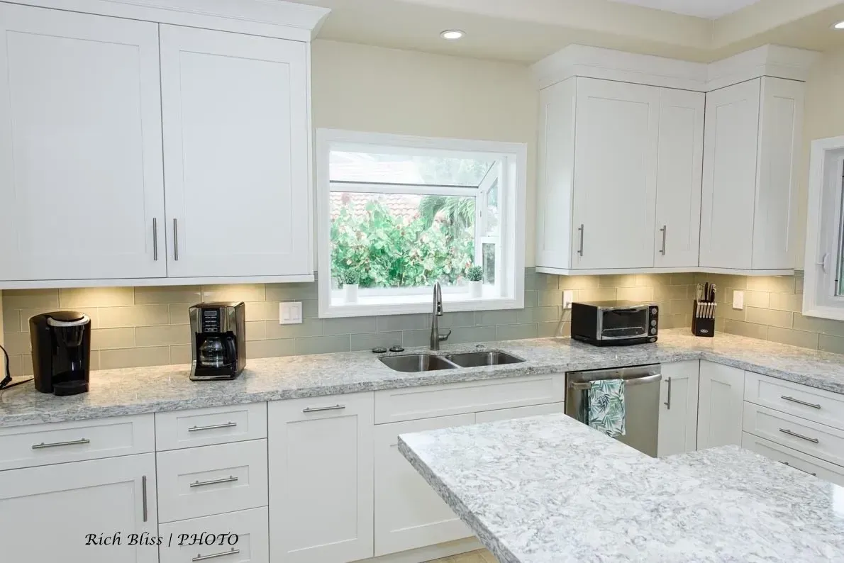 White kitchen with granite countertops, cabinets, appliances, and window.