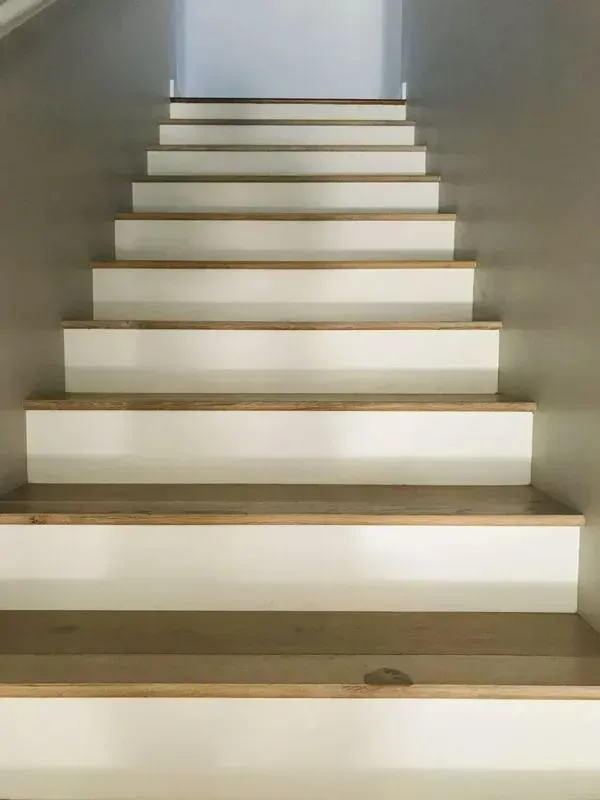 Staircase ascending. White risers with wood treads and wood trim, against neutral walls.