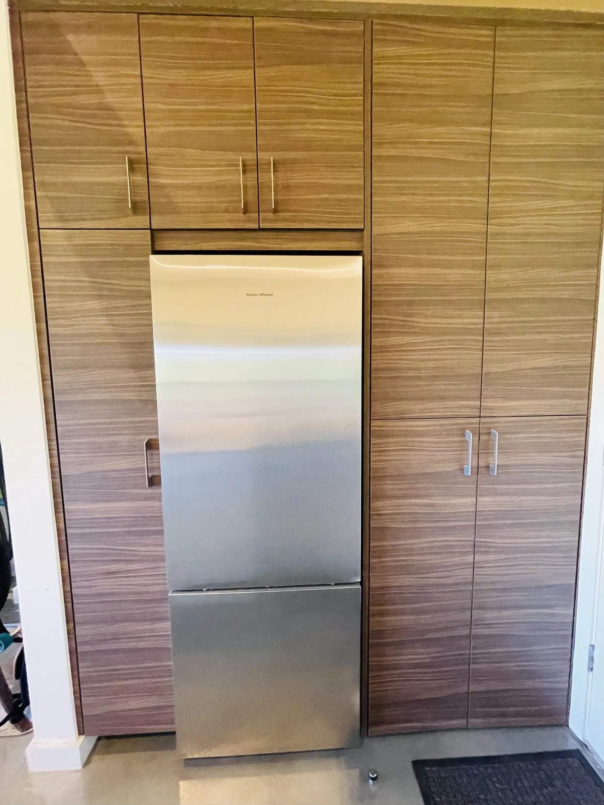 A stainless steel refrigerator is built into a wall with wooden cabinets.