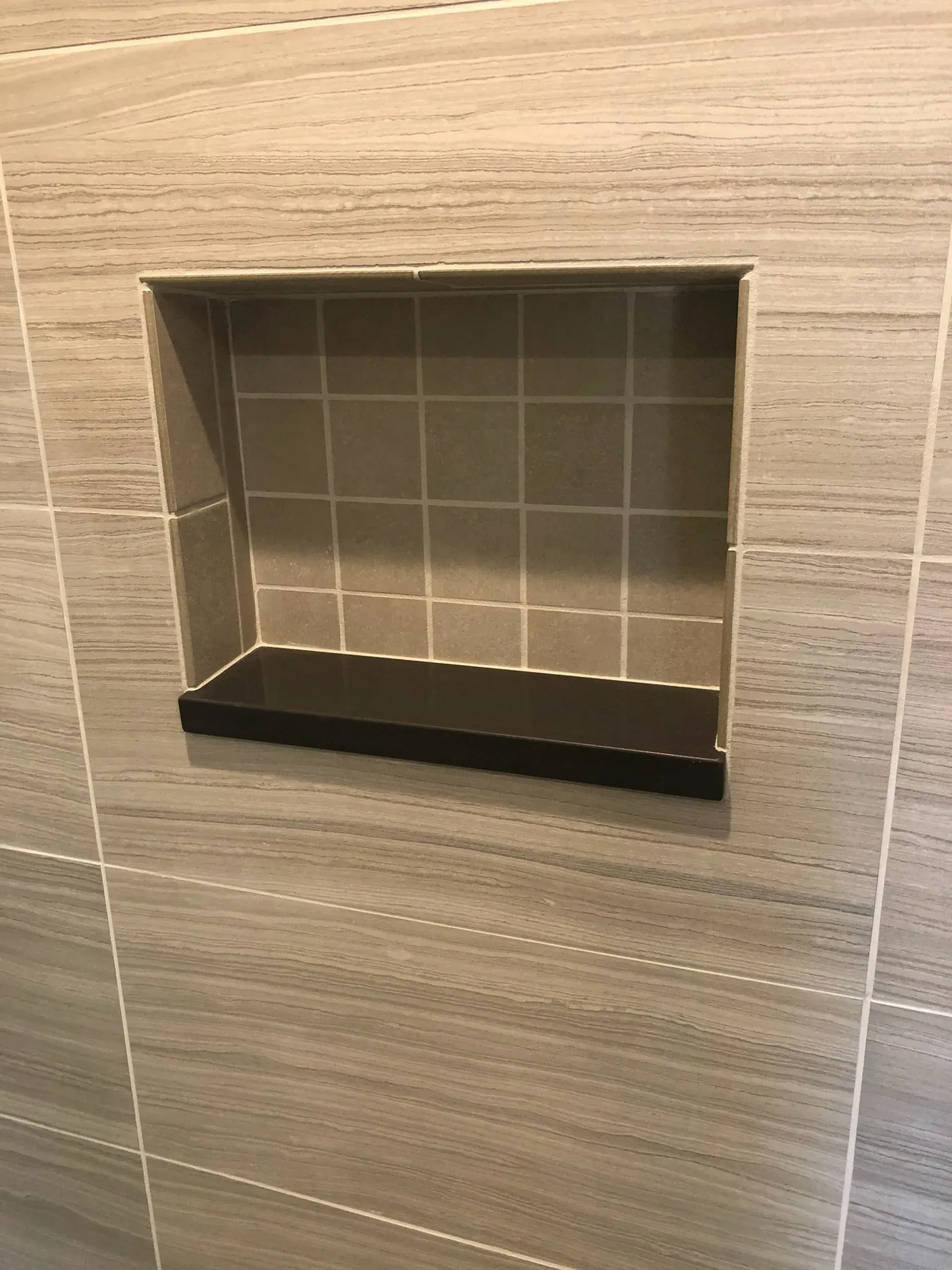A shower niche with a black shelf in a bathroom.
