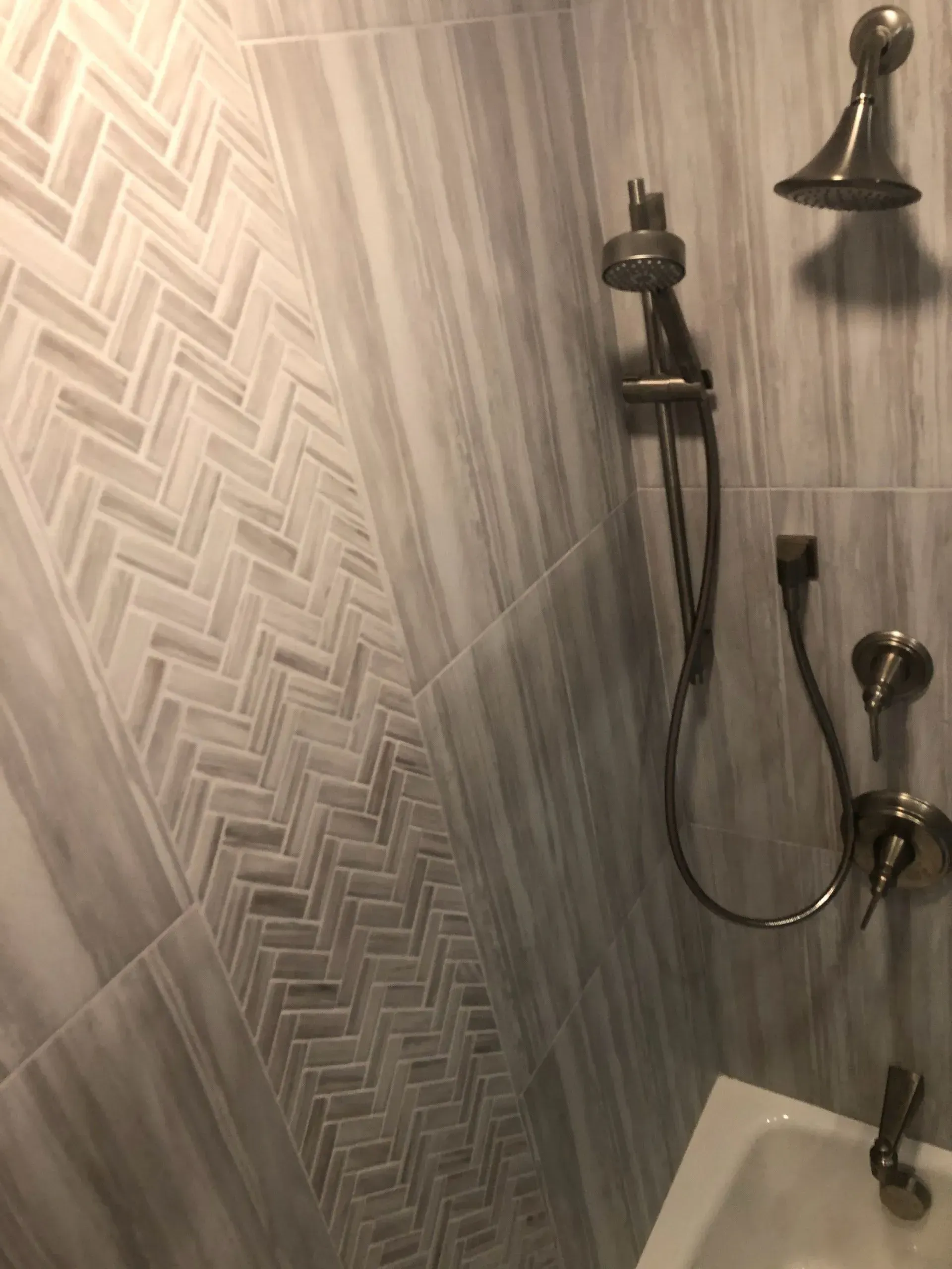 A shower with a bathtub and a shower head with a herringbone pattern on the wall.