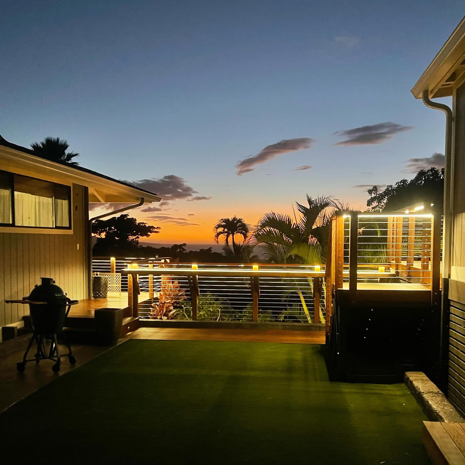 Sunset view from a deck with outdoor lighting, grill, and palm trees.