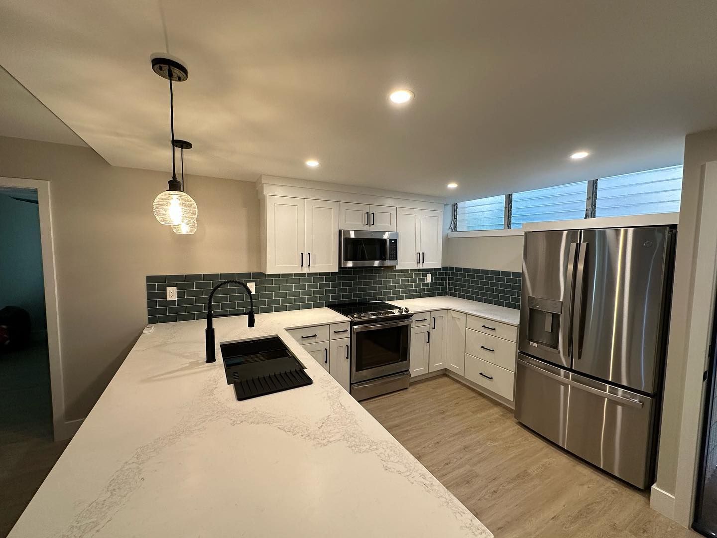 Modern white kitchen with quartz countertops, stainless steel appliances, and teal tile backsplash.