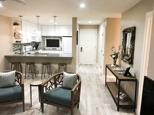 A living room with two chairs and a table and a kitchen in the background