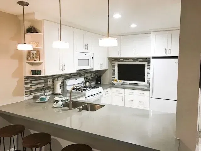 A kitchen with white cabinets , a sink , a refrigerator and a television.
