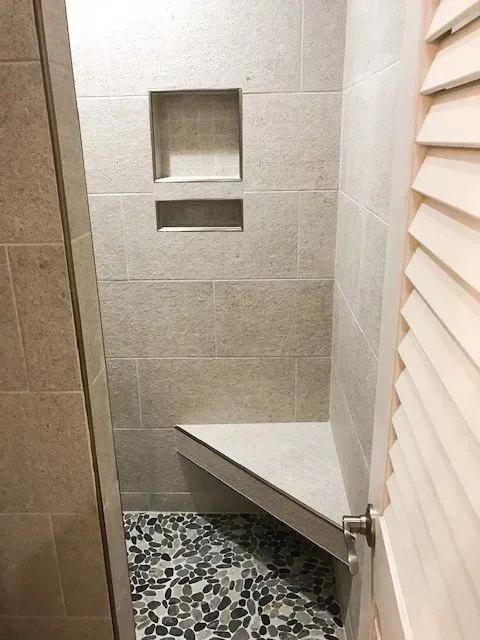 A shower with a bench and a shelf in the wall.