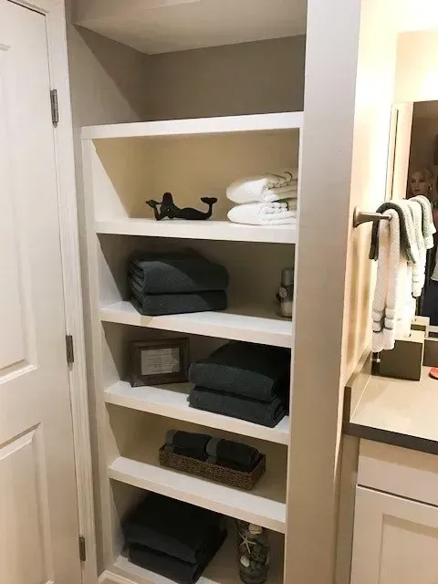 A bathroom with a closet filled with towels and a sink.