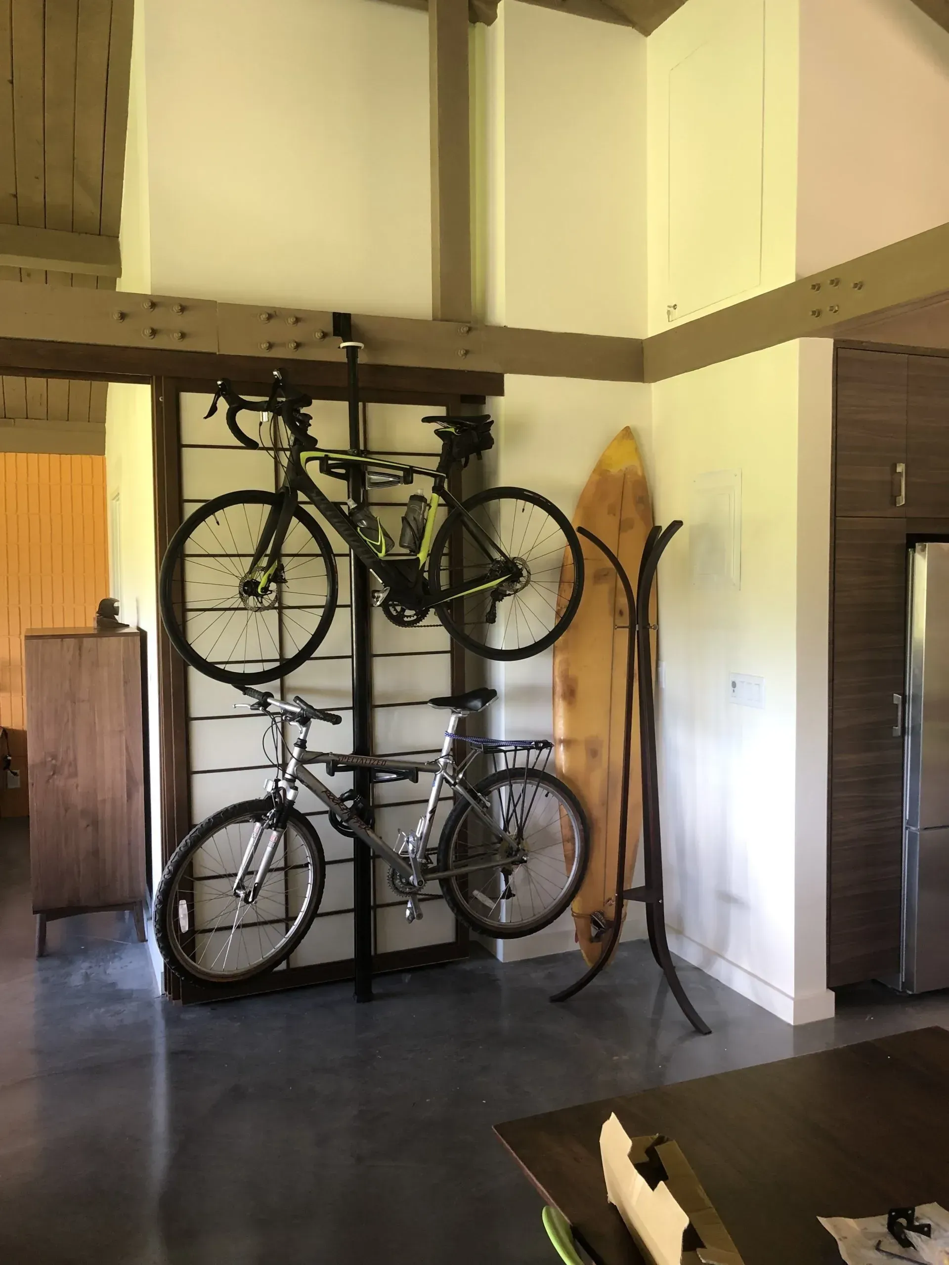 Two bikes are hanging on a wall next to a surfboard