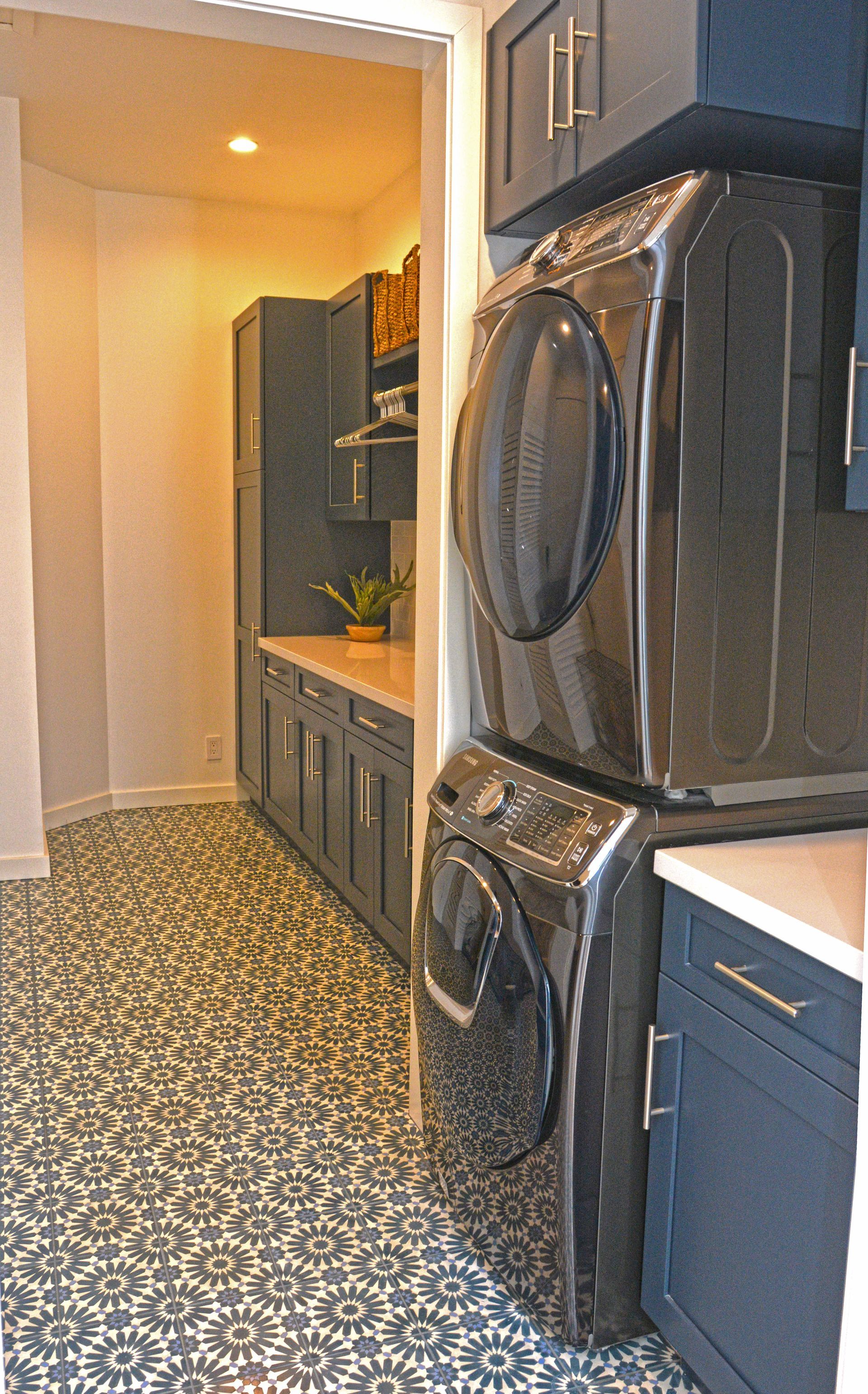 Laundry room with stacked black washer and dryer, blue cabinets, patterned tile floor.