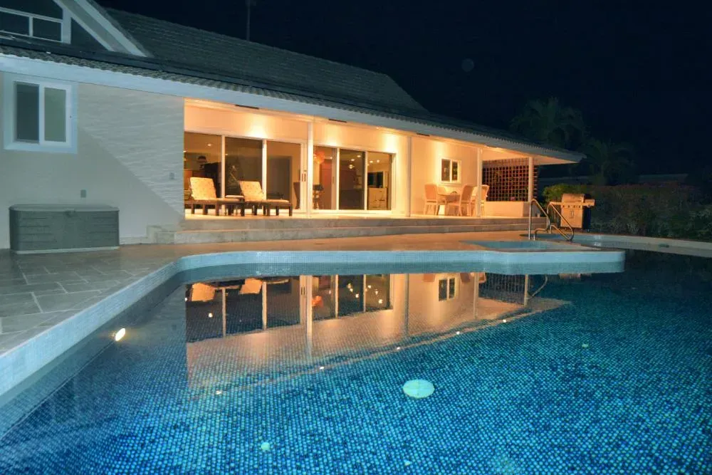 A large house with a swimming pool in front of it at night.