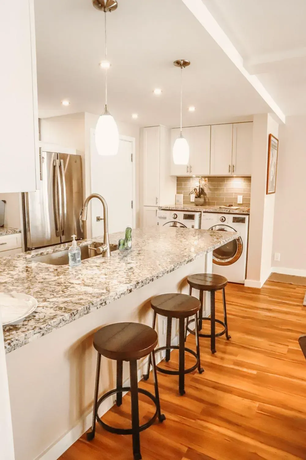 A kitchen with stools , a sink , a refrigerator and a washer and dryer.