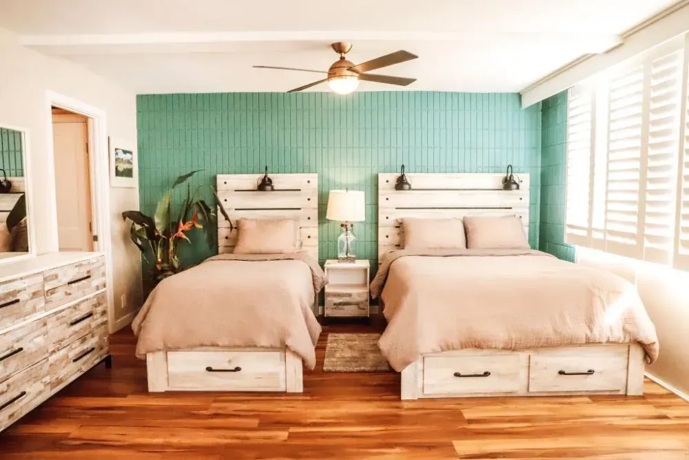 A bedroom with two beds , a dresser , a mirror and a ceiling fan.