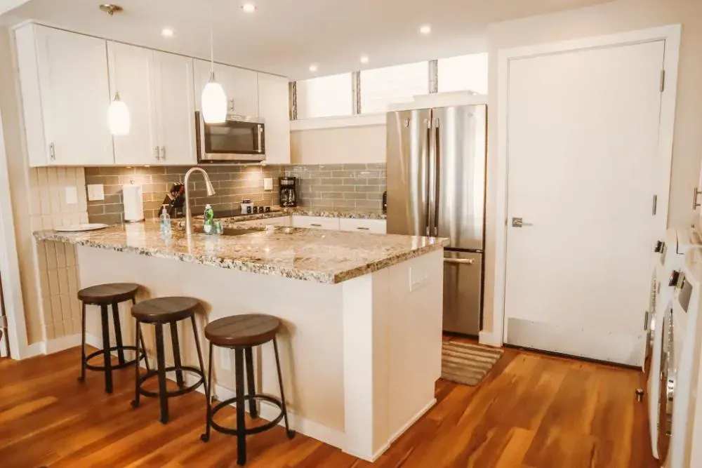 A kitchen with white cabinets , granite counter tops , stainless steel appliances and hardwood floors.