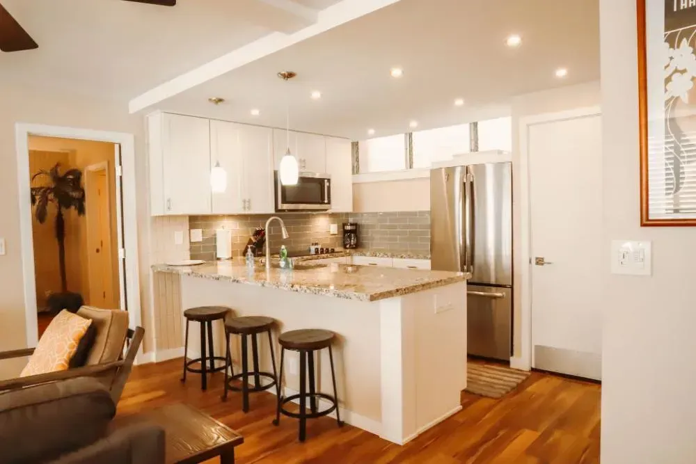 A kitchen with a large island and stools in a living room.