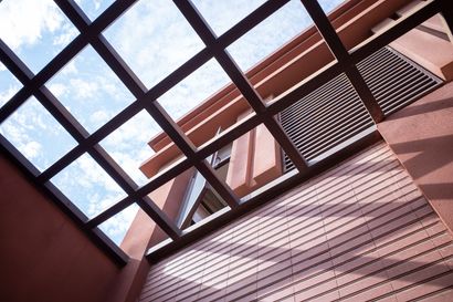 Brown wooden lattice roof over a light-colored building with blue sky peeking through the roof.