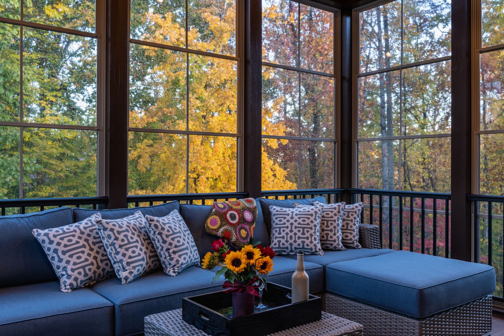 Screened porch with blue sectional sofa, autumn foliage view. Sunflowers on a tray.