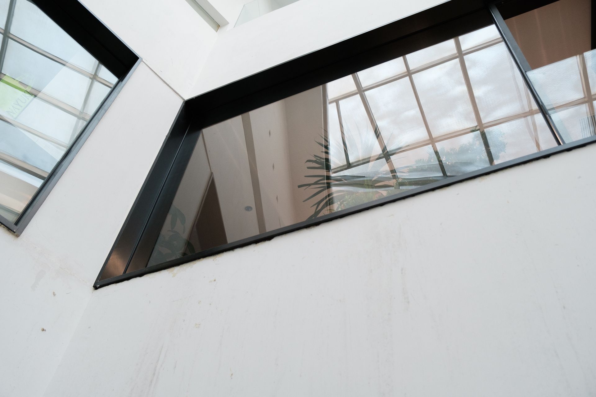 Interior corner with white walls, black-framed windows reflecting a cloudy sky.