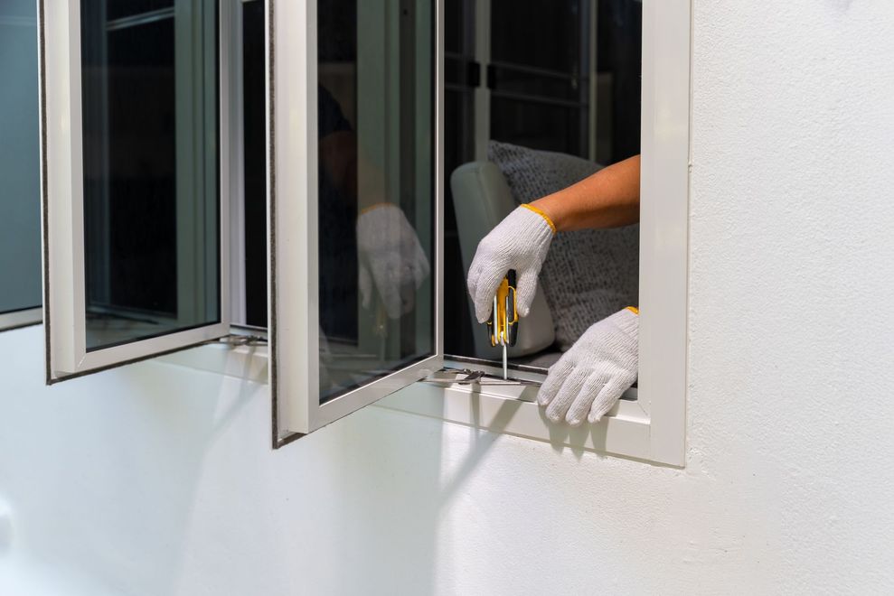 Person wearing gloves using a screwdriver on a window, indoors.
