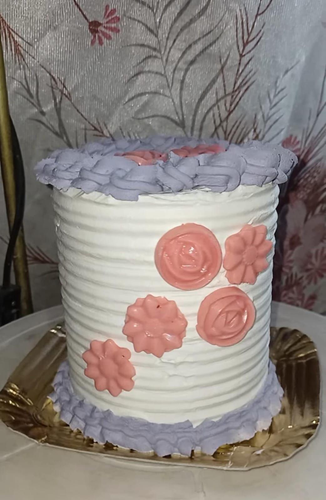 Pastel decorado con glaseado blanco, detalles de flores rosas y bordes morados.