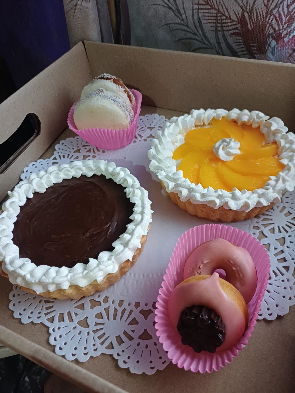 Caja de pasteles variados: tarta de chocolate, tarta de melocotón, macarons y donuts glaseados.